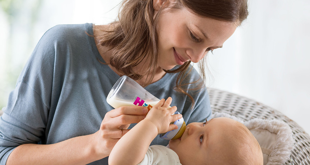 A woman in a blue shirt is feeding a baby with a bottle.