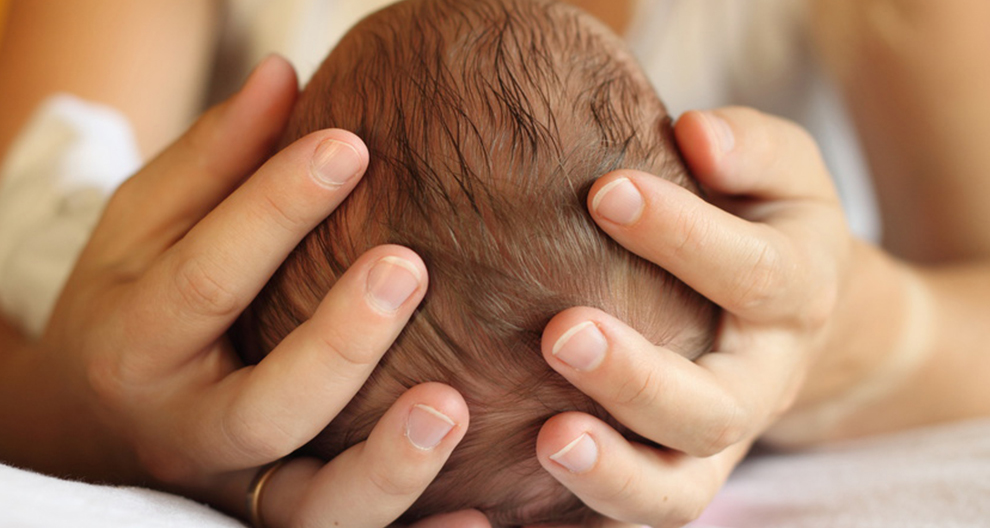 A close-up of a person's hands gently cradling a baby's head.