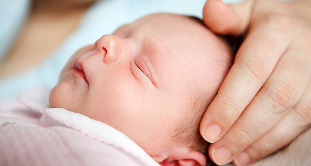 A close-up of a newborn baby's face, partially cradled by a hand.
