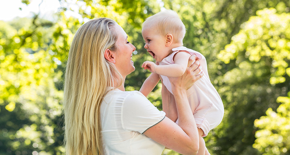 A woman holds a baby in an outdoor setting.
